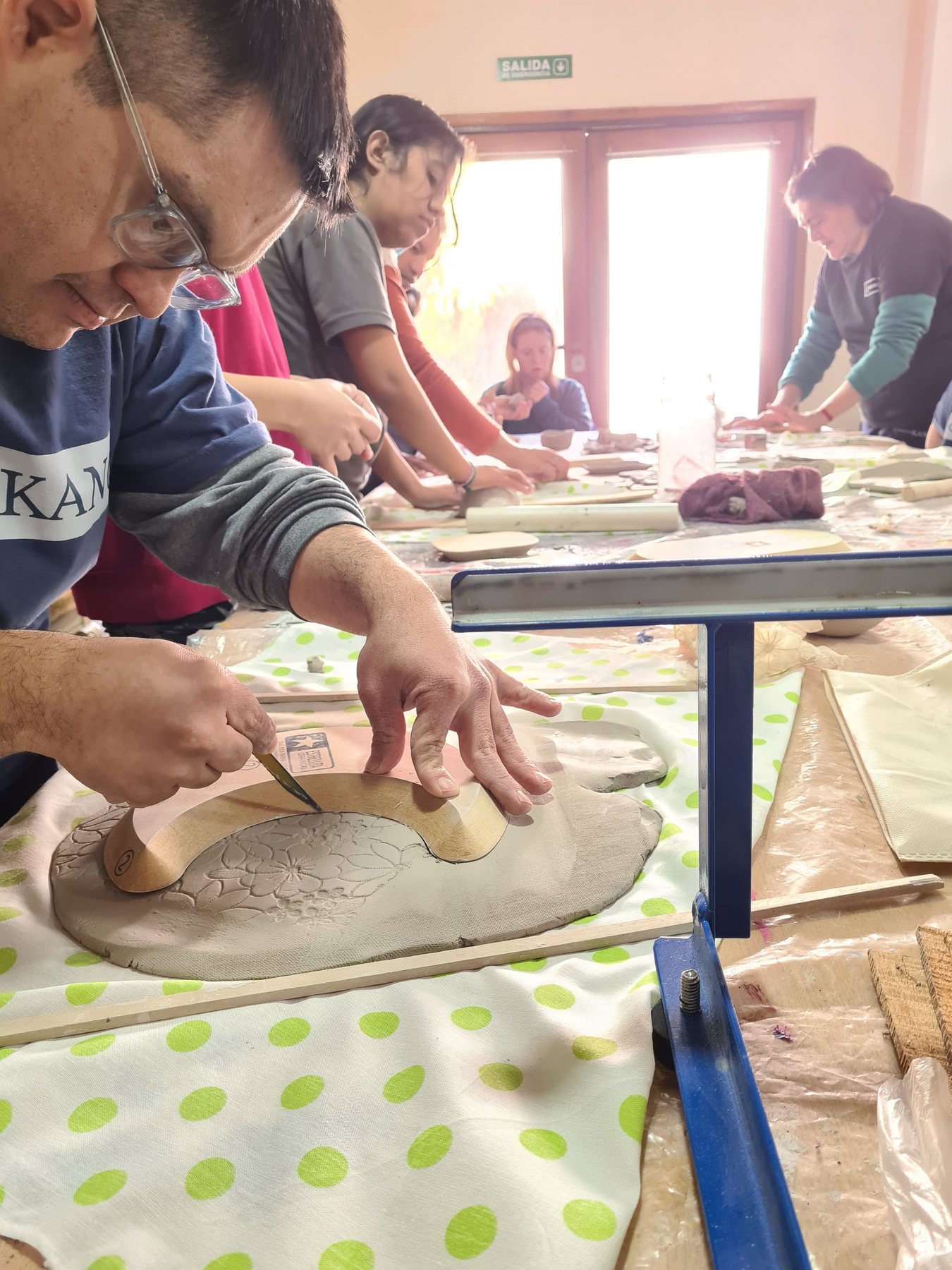 Manos trabajando una plancha de arcilla sobre la mesa del taller de cerámica.