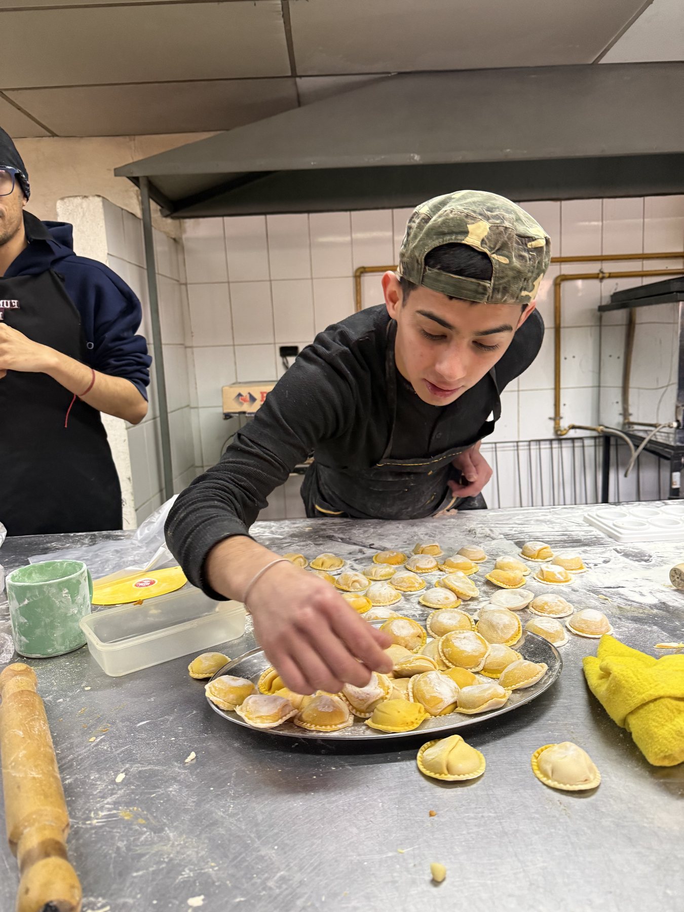 Manos acomodando pastas rellenas recién armadas sobre una bandeja.