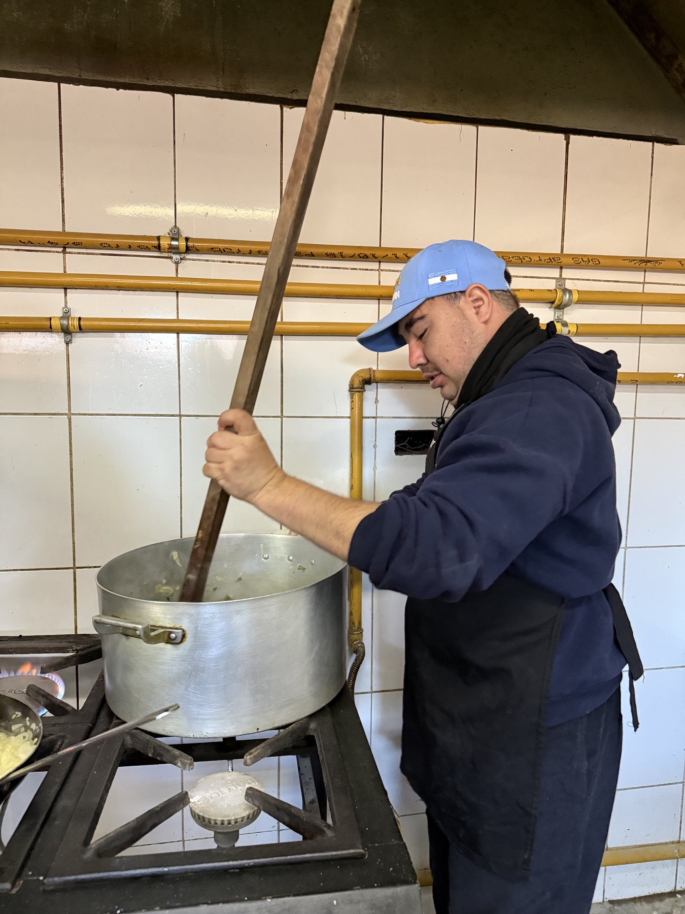Un trabajador revuelve una olla grande sobre la hornalla de la cocina.
