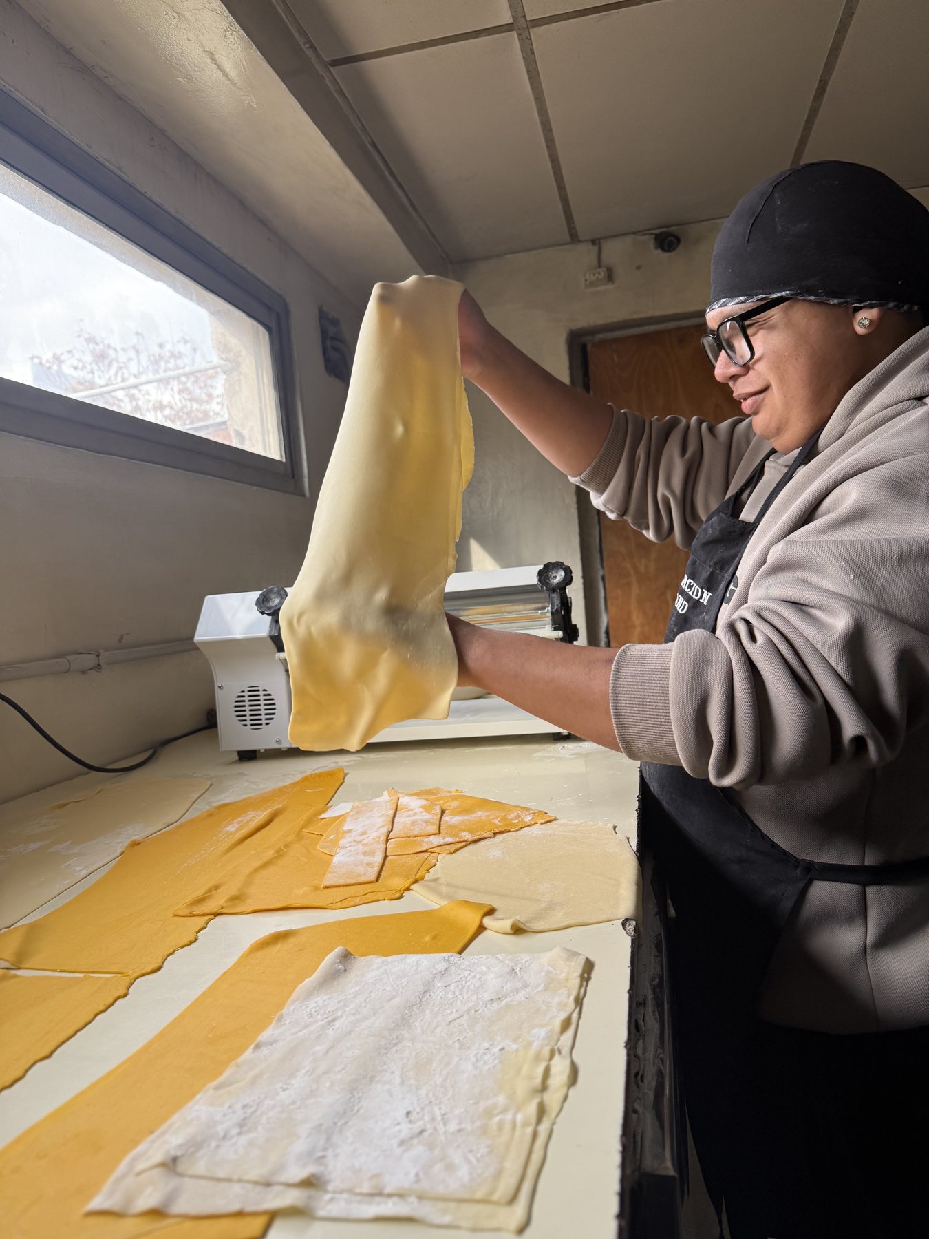 Una trabajadora pasa una lámina de masa amarilla por la máquina de pastas.